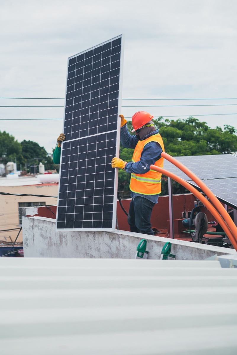Installateur montant un panneau solaire sur le toit d'une maison en ville